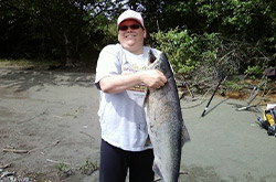 Person smiling while holding a large salmon fish